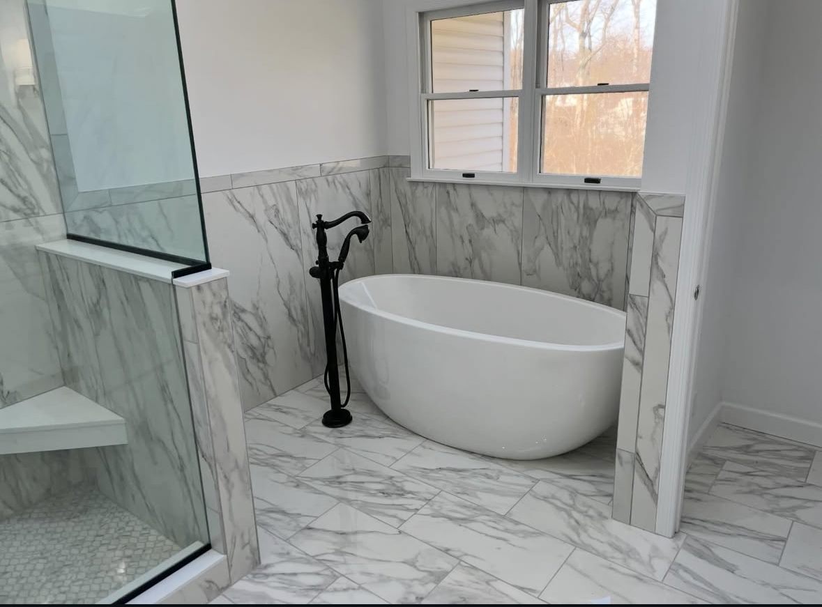 Primary bathroom with marble-look walls and floor around a freestanding soaking tub